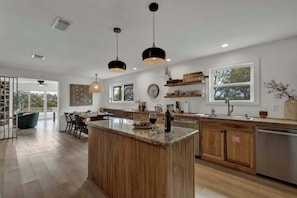 Una cocina moderna con una isla central, armarios de madera, iluminación colgante y ventanas amplias.