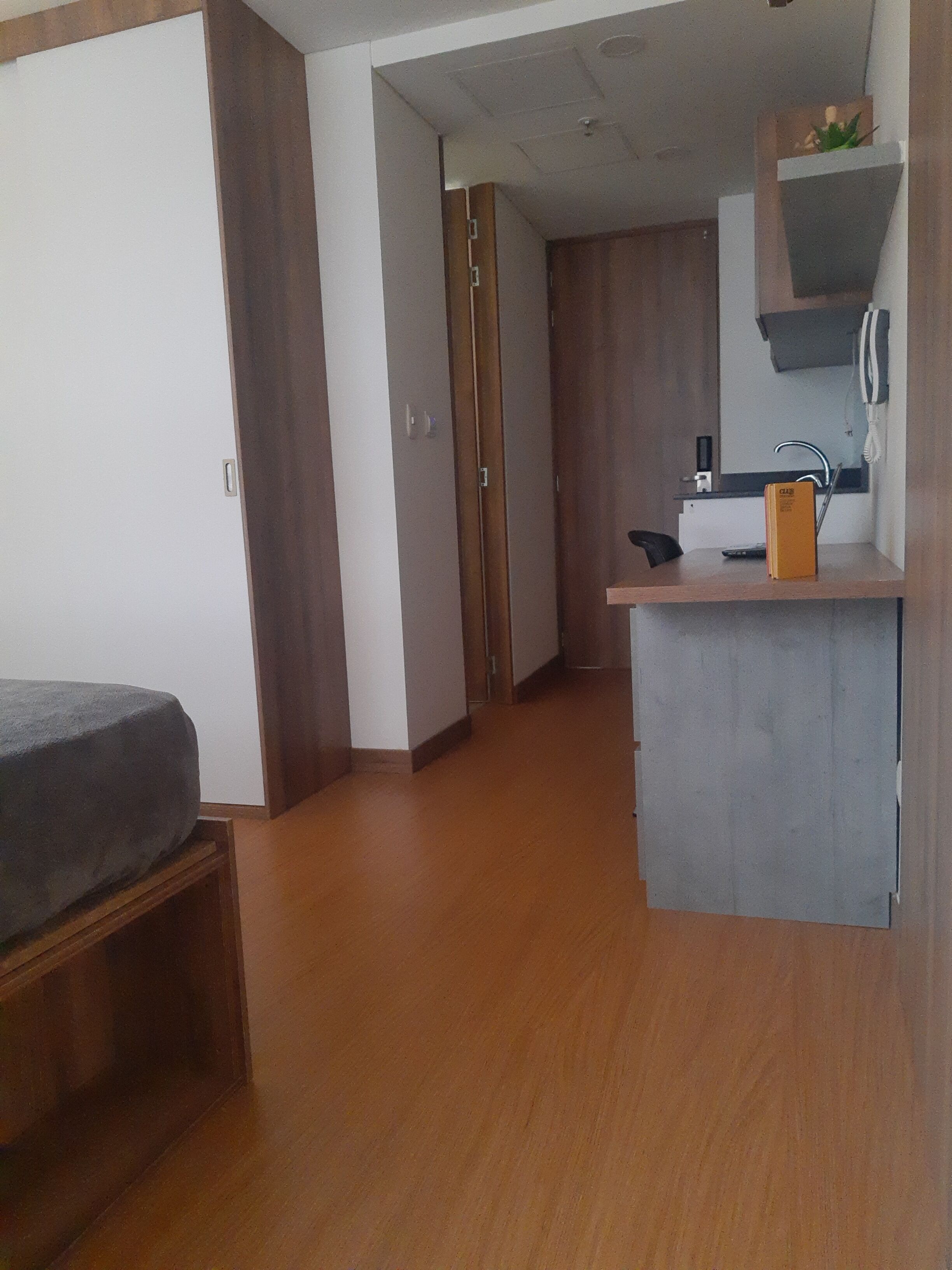 Una habitación funcional con cama, kitchenette y armario de madera.