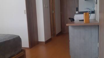 Una habitación funcional con cama, kitchenette y armario de madera.