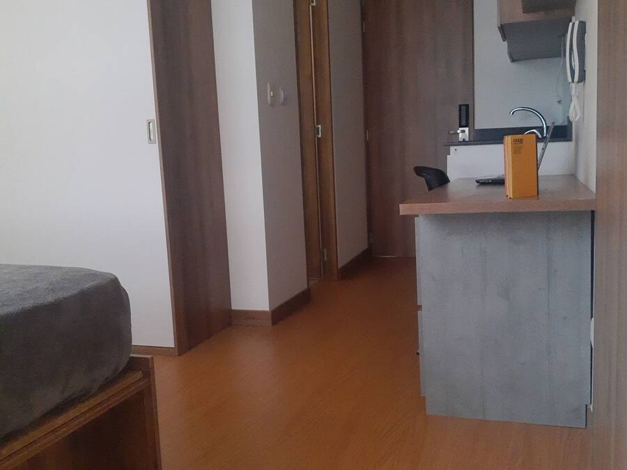Una habitación funcional con cama, kitchenette y armario de madera.