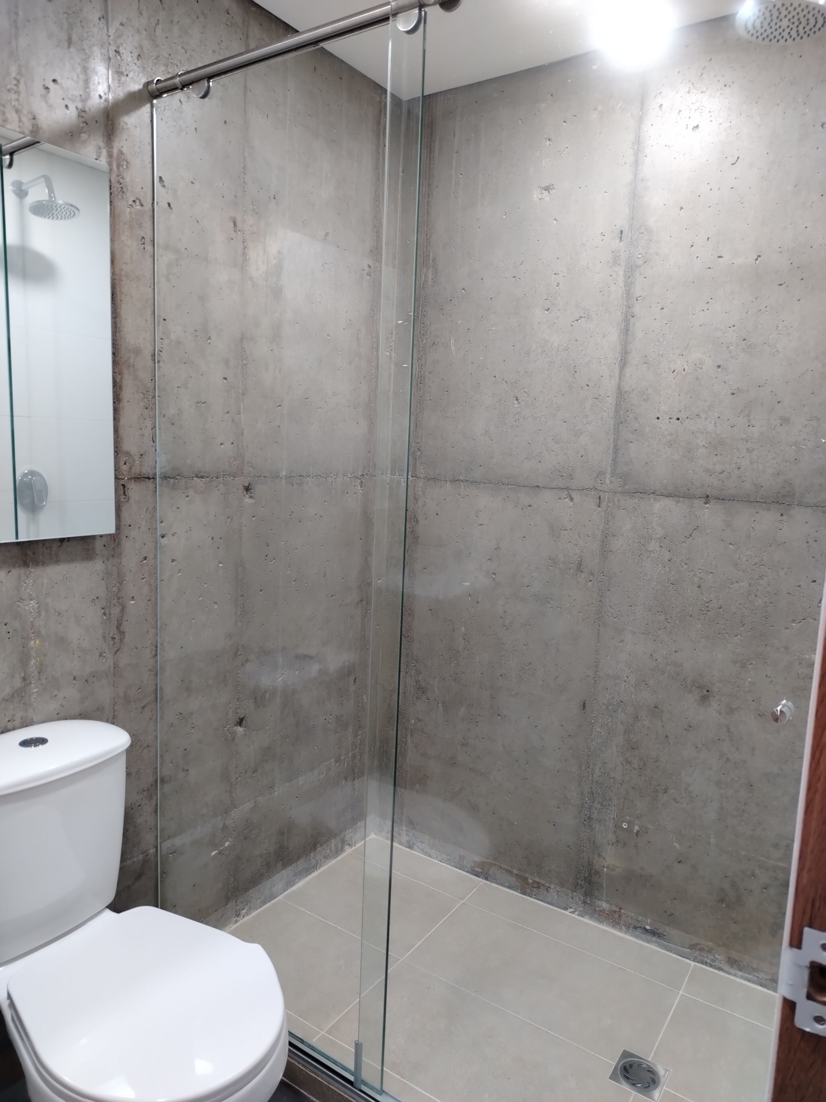 A shower with a glass door, a white toilet, and a tiled floor.