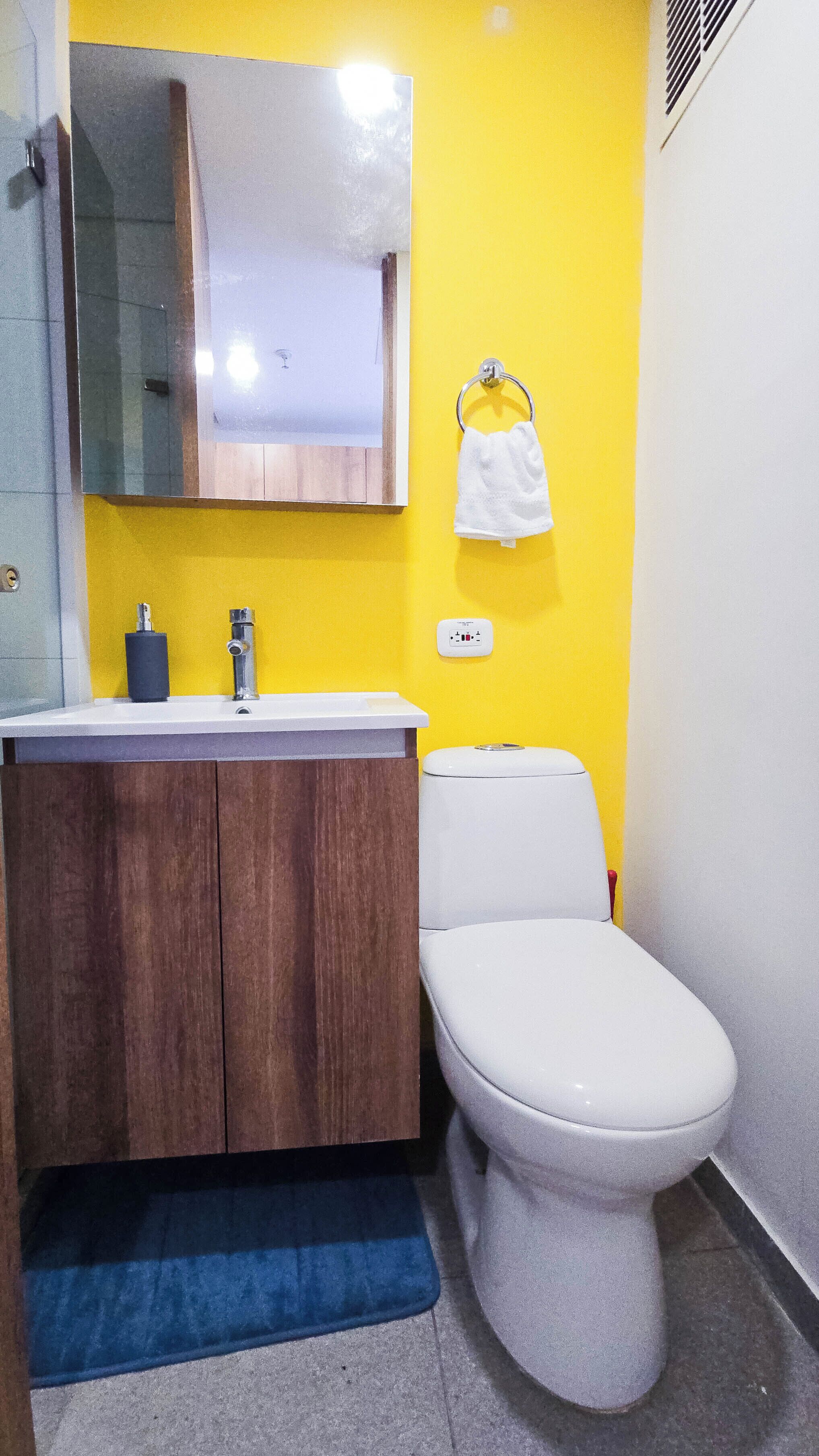 Une salle de bain avec un mur jaune, des toilettes blanches et des meubles en bois.