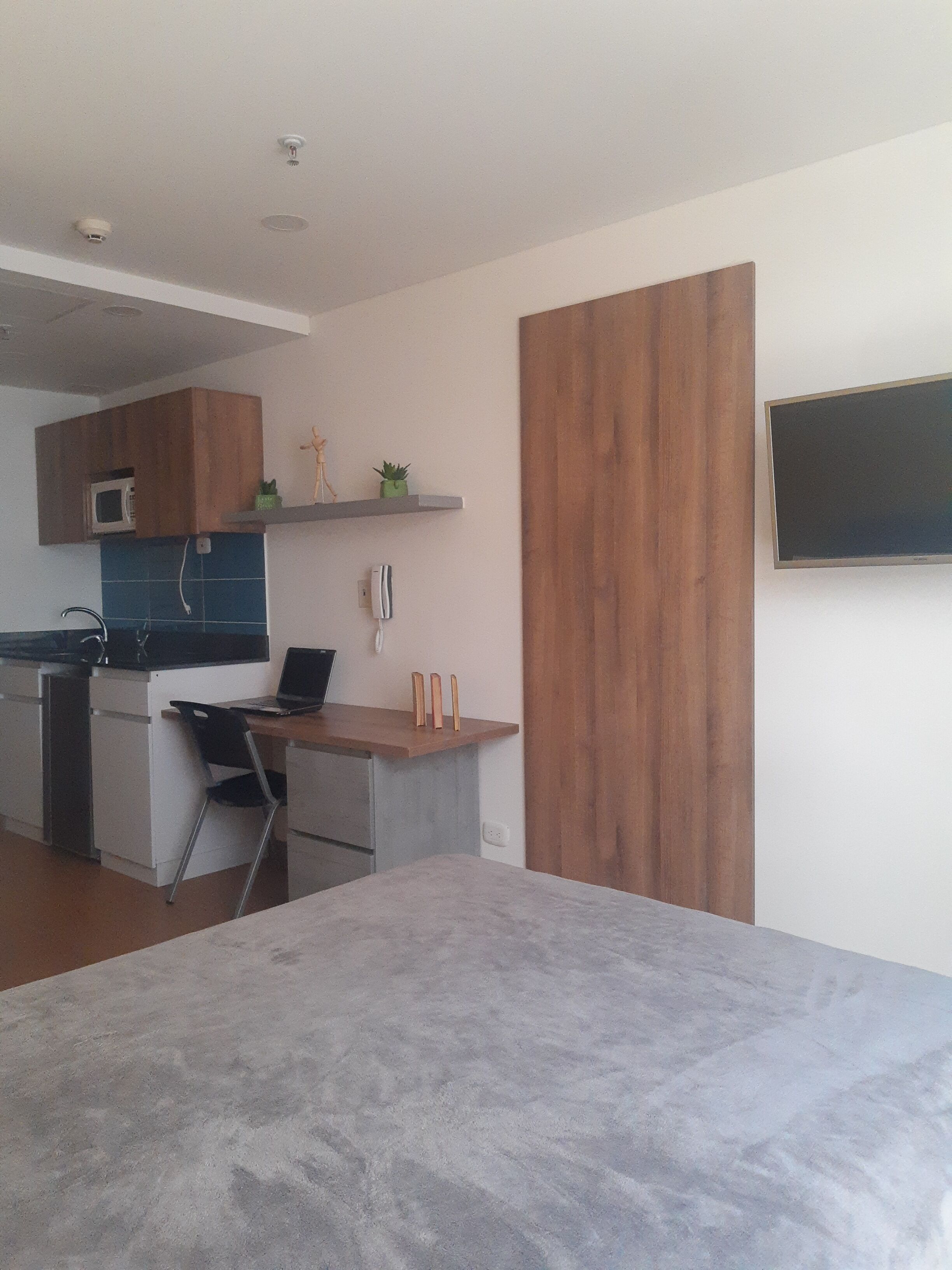 Una cocina moderna con microondas, una laptop sobre la encimera y un armario de madera arriba.