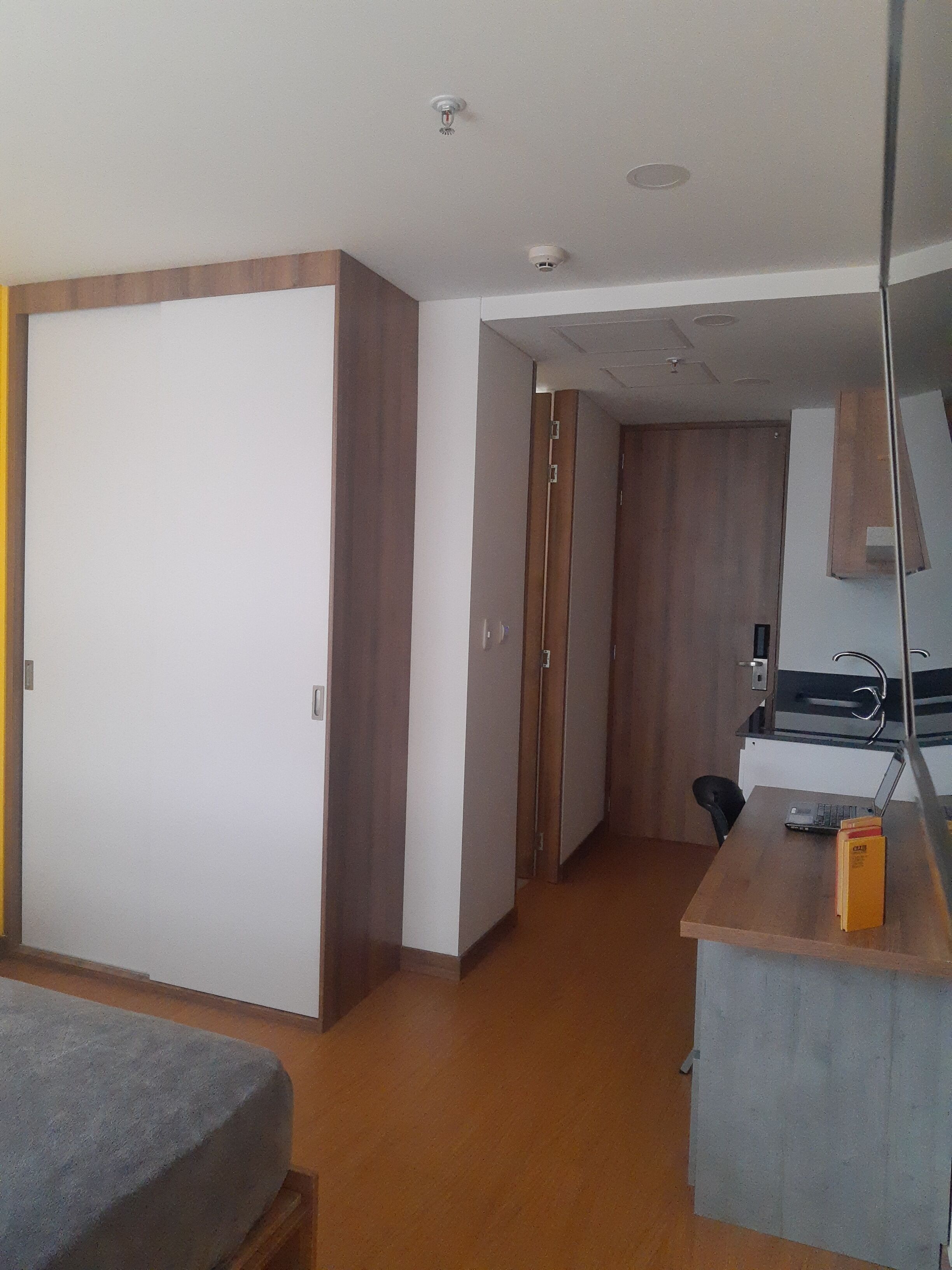 Una habitación de hotel con cama, un escritorio con una computadora portátil, una silla y un armario.