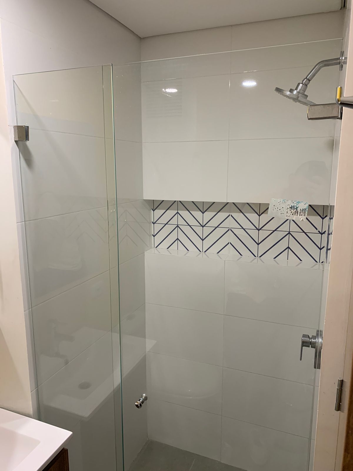 Een moderne badkamer met een douchecabine van glas, een wit wastafeltje en een betegelde spatwand.