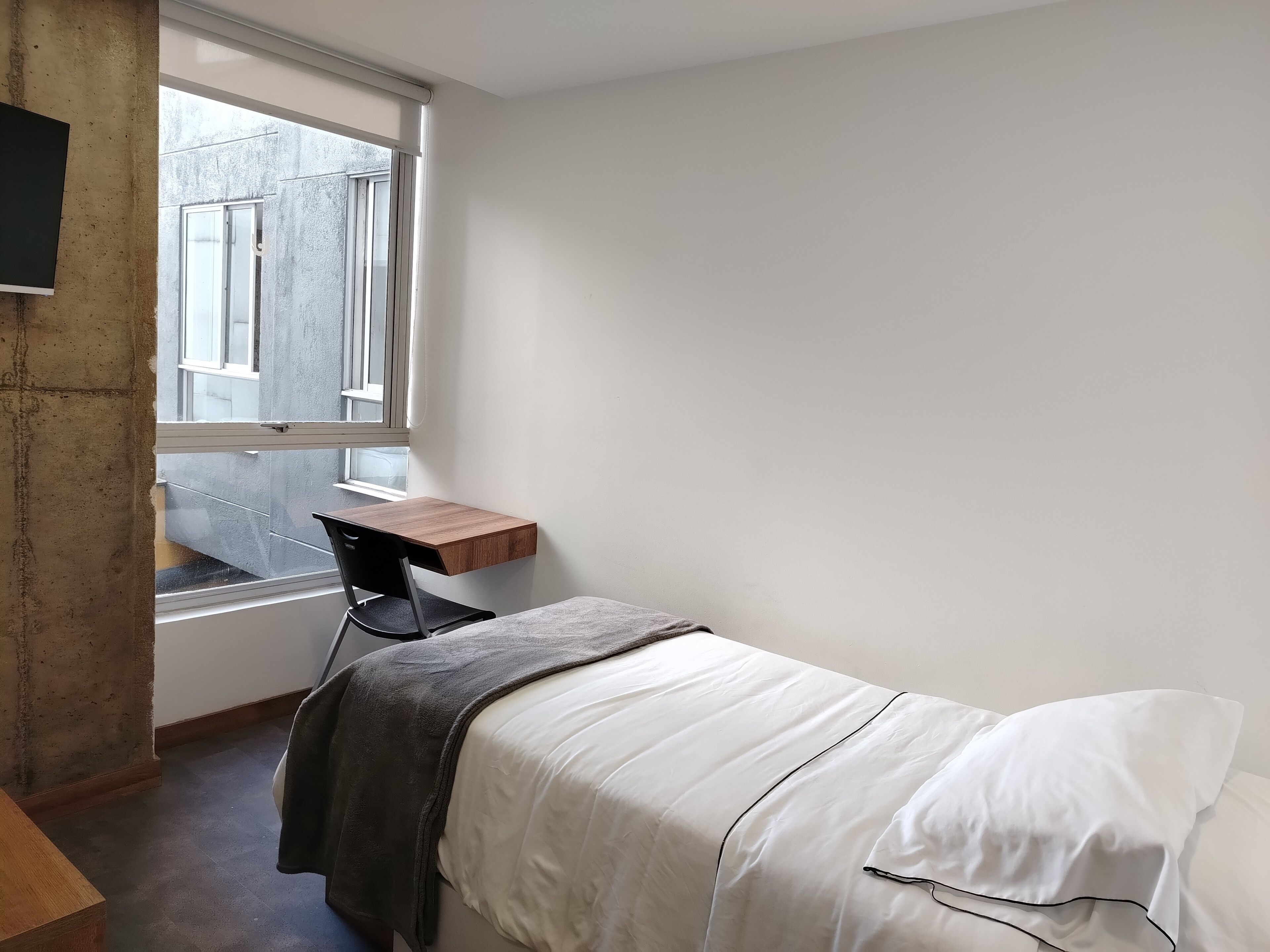 A small, simple room with a bed, a desk, and a window.