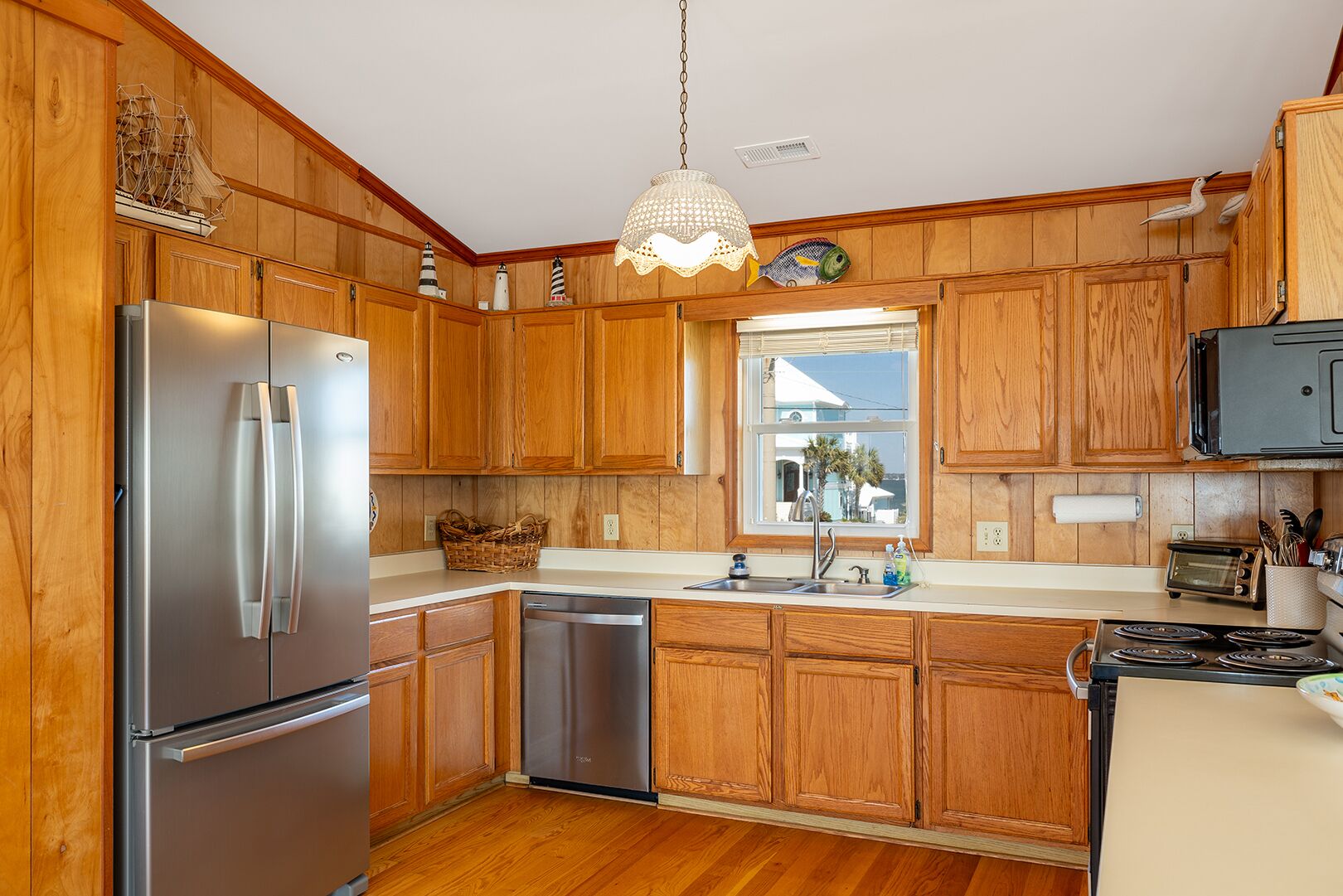 A kitchen with wooden cabinets, stainless steel appliances, a window with a view, and a hanging light fixture.