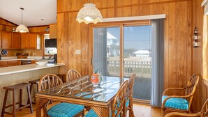A wooden-paneled room with a glass dining table, chairs, and a large sliding glass door leading to a balcony. - Adjust Your Focus, Almost Oceanfront Duplex in Emerald Isle, NC! (Emerald Isle)