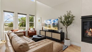 Una sala de estar moderna con un amplio sofá modular, un televisor de pantalla plana, una chimenea y ventanas grandes que ofrecen vistas al exterior.