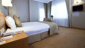 A hotel room with a large bed, a bedside table with a telephone, a small table with a vase, and a television mounted on the wall. - SEFA 2 BUTİK HOTEL (Corlu)