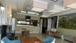 A modern living room with a wooden dining table, blue upholstered chairs, a bar area with a stone wall, and a large window with bamboo plants. - SEFA 2 BUTİK HOTEL (Corlu)