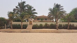 A beachfront property with a large house, palm trees, and a sandy beach.