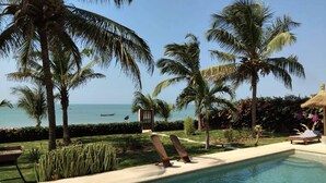 A pool area with lounge chairs, palm trees, and a view of the ocean.
