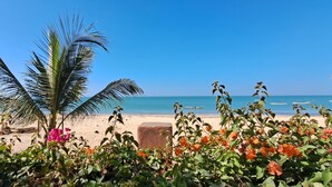 A beach with palm trees and flowers in the foreground, a sandy beach, and the ocean in the background.