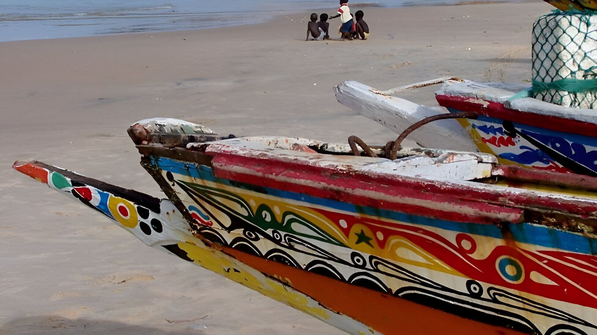 A colorful boat with intricate designs on a sandy beach.