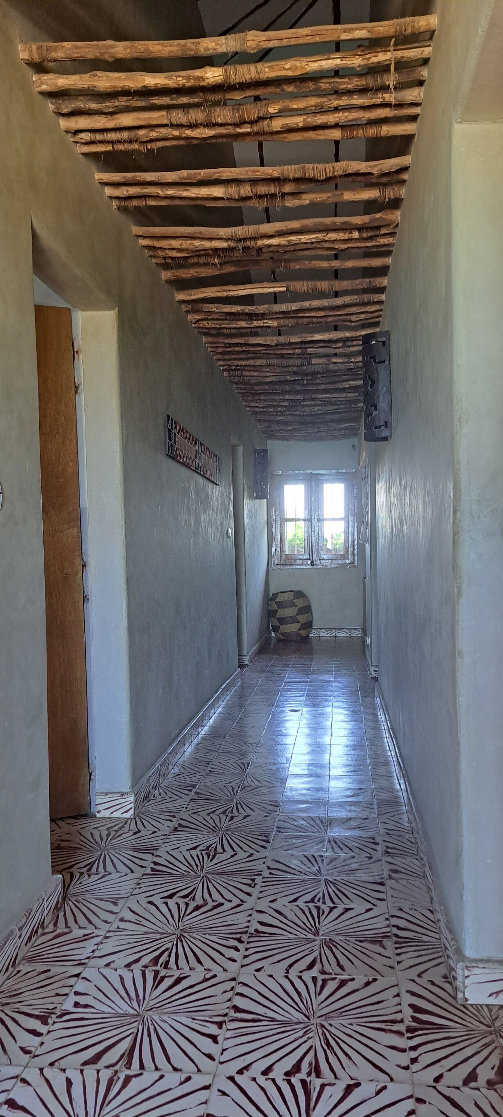 A hallway with a patterned floor, wooden ceiling beams, and a window with natural light.