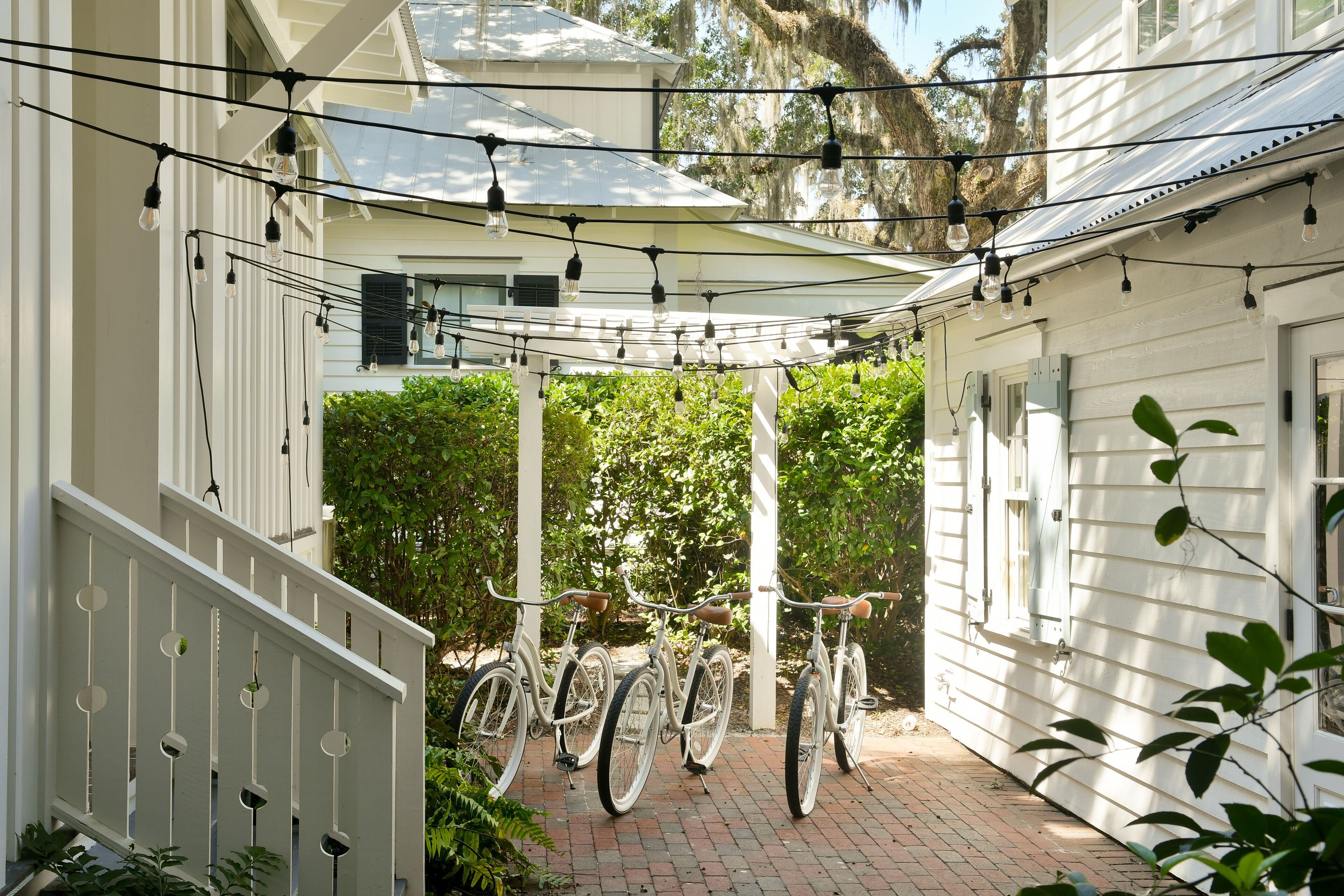 A covered patio area with bicycles, string lights, and a brick pathway.