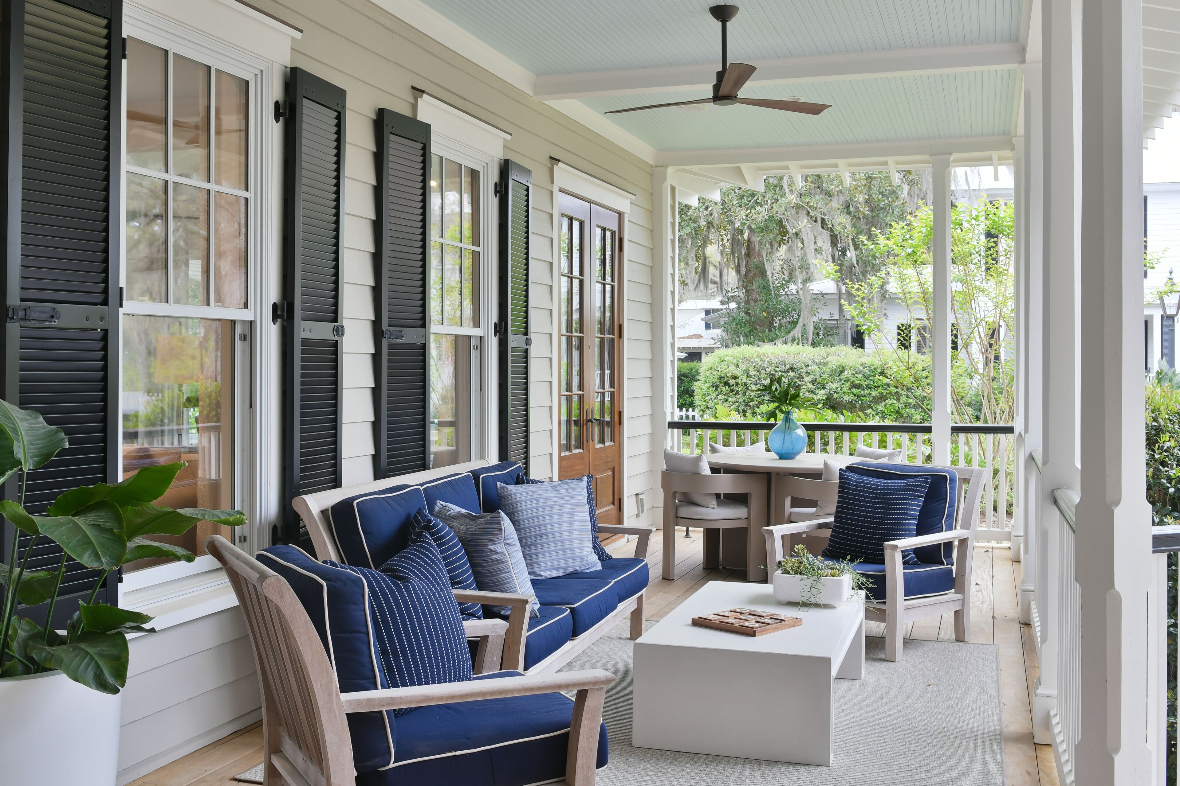 A covered porch with a blue sofa, white coffee table, and chairs.