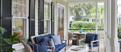 A covered porch with a blue sofa, white coffee table, and chairs.