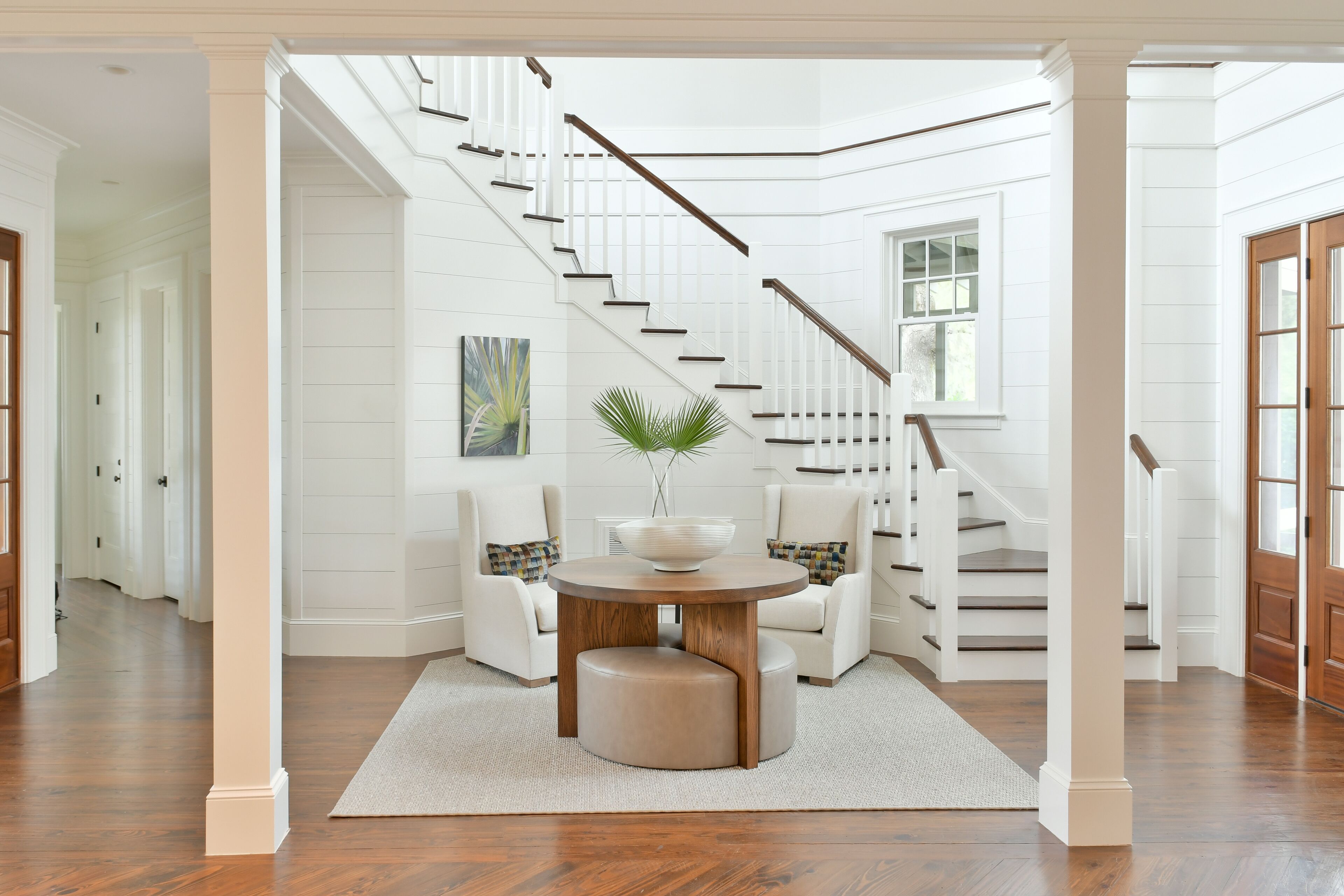 A spacious foyer with a wooden staircase, a round table with a bowl, and two armchairs.