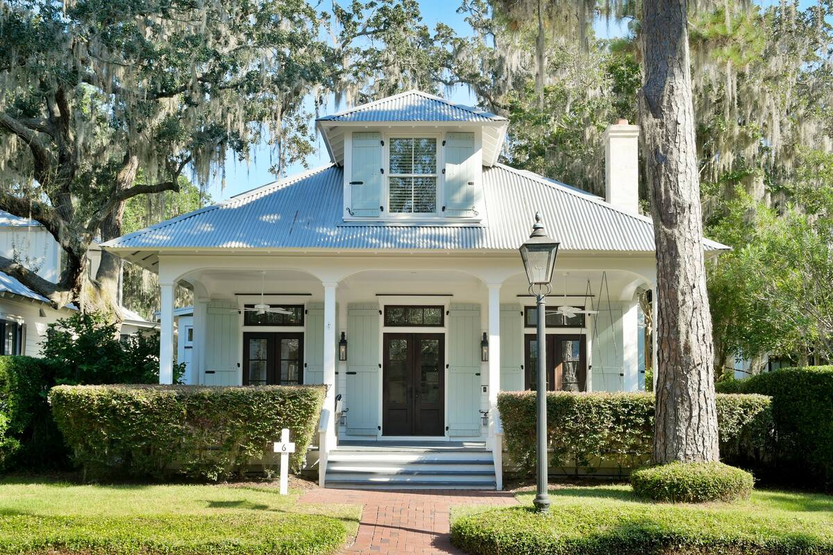 Een wit huis in koloniale stijl met een blauw dak, een veranda en een schoorsteen.