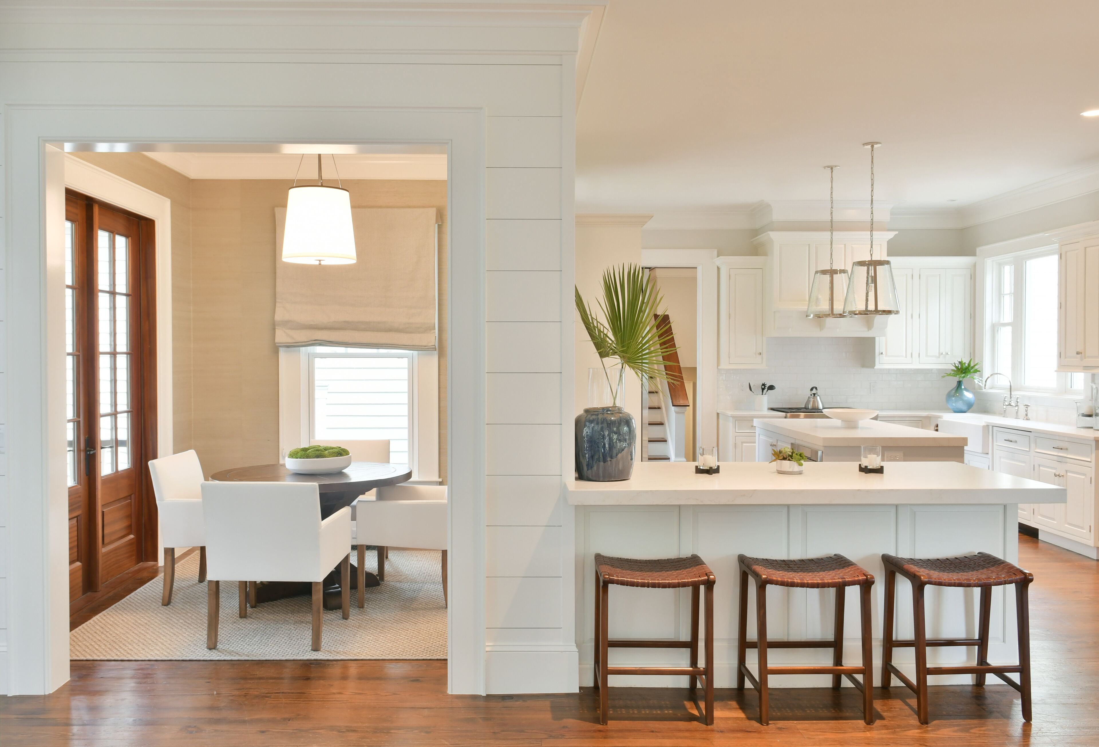 A modern kitchen with white cabinetry, a central island with stools, and pendant lighting.