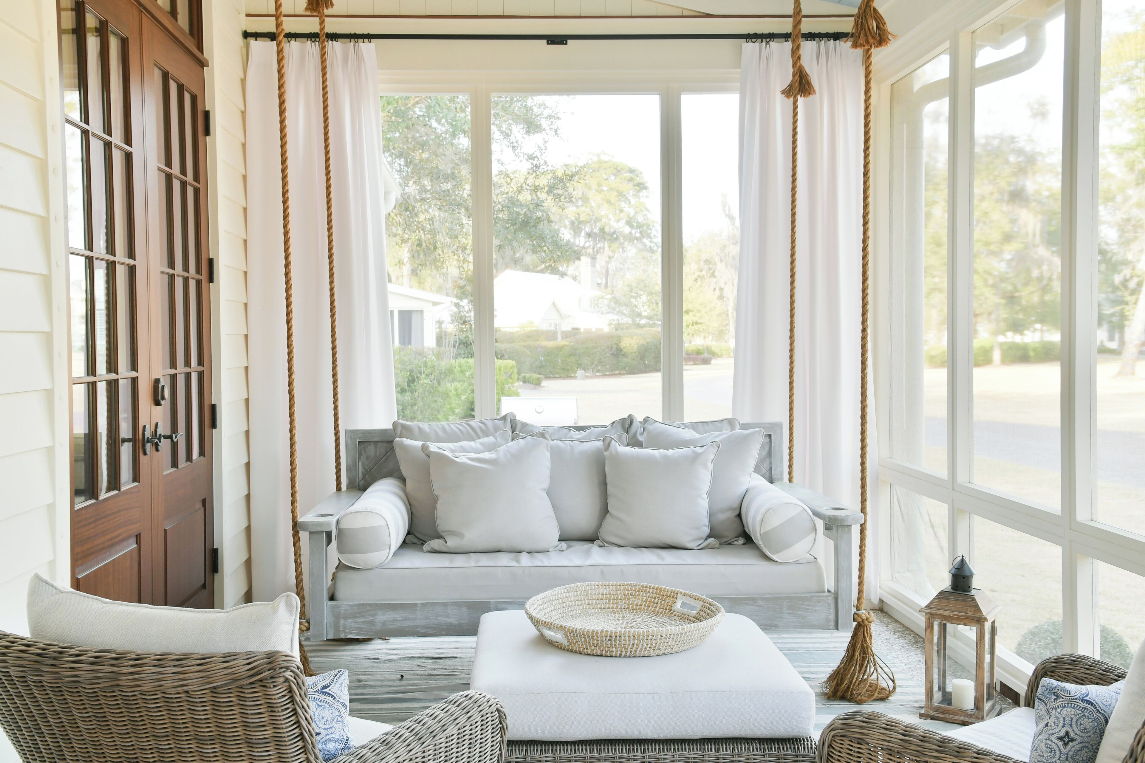 A cozy porch with a cushioned seating area, a wicker chair, and a wicker basket.