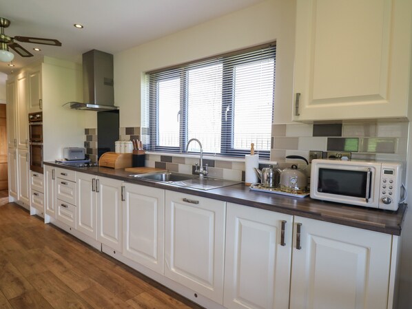 A modern kitchen with white cabinetry, a stainless steel sink, a microwave, and a window with blinds.
