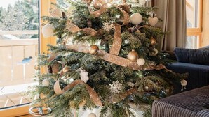 A Christmas tree decorated with ornaments and ribbons, placed in a room with wooden flooring and a blue armchair. - Chalet Familial vue Mont Blanc à 100m des Pistes de ski (Taninges)