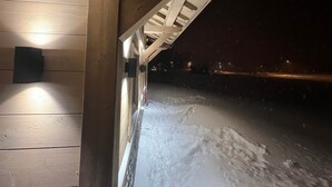 A snow-covered outdoor area under a wooden structure with a light fixture on the wall.