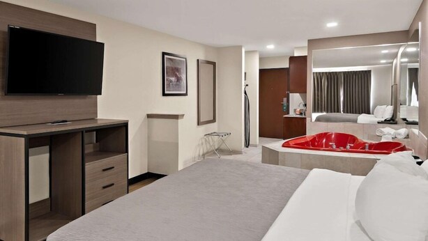 A modern hotel room with a large bed, a desk with drawers, a flat-screen TV mounted on the wall, a red bathtub, and a large mirror. - Quality Inn & Suites Weatherford, TX (Weatherford)