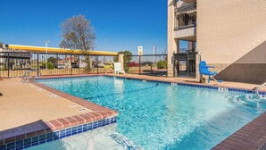 A swimming pool with a brick edge, a fenced area, and a building in the background. - Quality Inn & Suites Weatherford, TX (Weatherford)