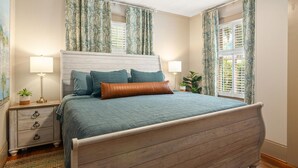 A bedroom with a wooden bed, two bedside tables with lamps, a nightstand with drawers, and a window with curtains.