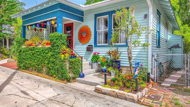 A house with a blue exterior, a front porch with potted plants, and a large decorative sun on the wall.
