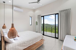 Un dormitorio con una cama grande, ventilador de techo y vistas a un paisaje verde a través de una puerta corrediza de vidrio.