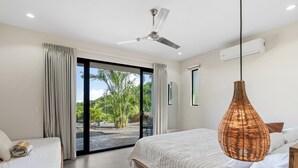 A bedroom with a bed, a ceiling fan, a large window with curtains, and a view of greenery outside.