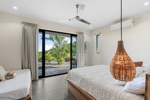 Un dormitorio con cama, ventilador de techo, ventana grande con cortinas y vista a zonas verdes.