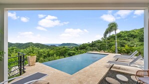 A swimming pool with lounge chairs and a view of lush greenery and hills.