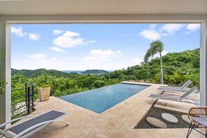 Piscina con sillas de descanso y vistas a vegetación exuberante y colinas.