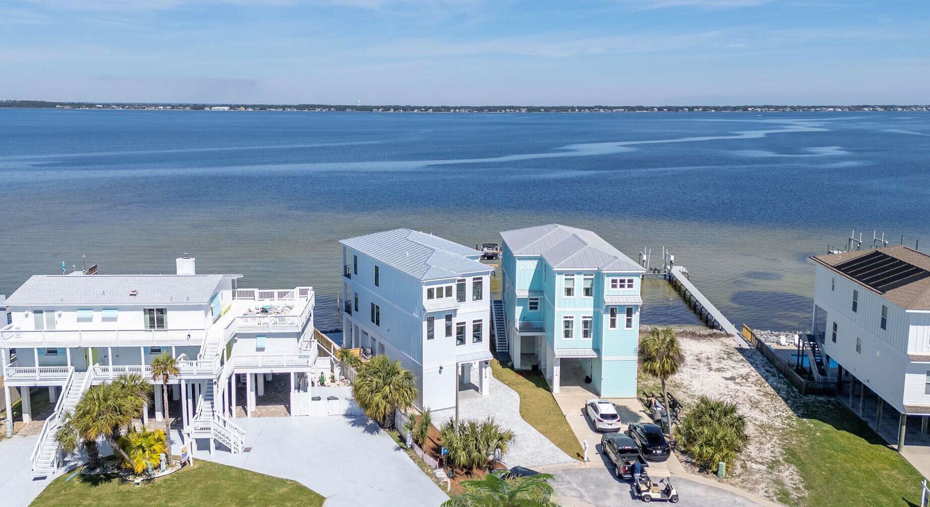 A coastal residential area with houses near the water, featuring a dock and a clear view of the ocean.