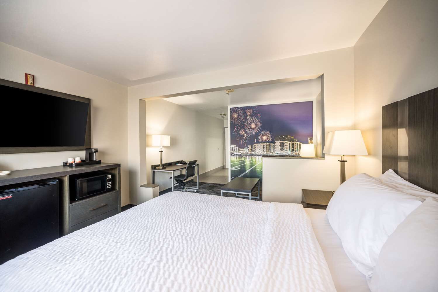 A hotel room with a bed, a desk, a chair, a television, a coffee machine, and a mirror.