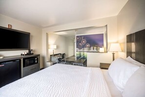 Habitación de hotel con cama, escritorio, silla, televisor, cafetera y espejo.
