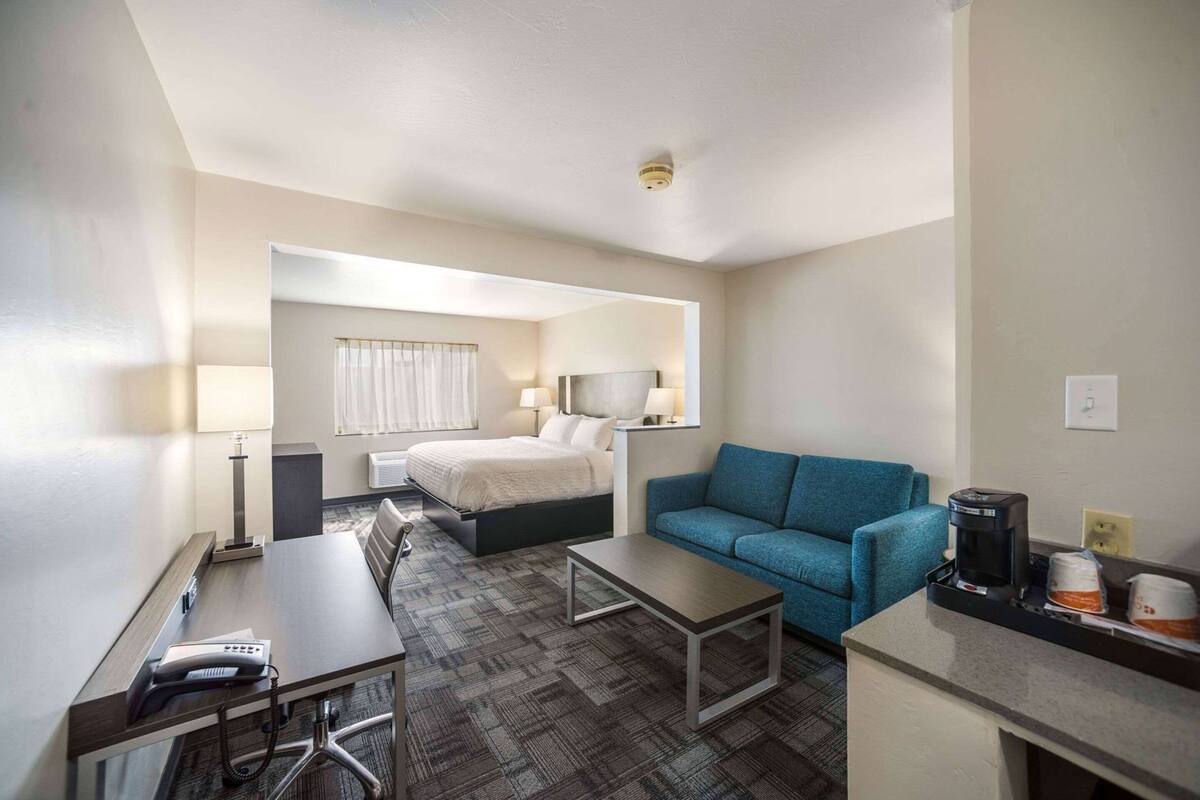 Une chambre d’hôtel avec un lit, un canapé bleu, un bureau avec un téléphone et une machine à café.