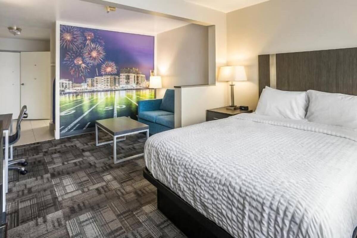 Une chambre d’hôtel avec un grand lit, un bureau, une chaise, une petite table et une fresque murale.