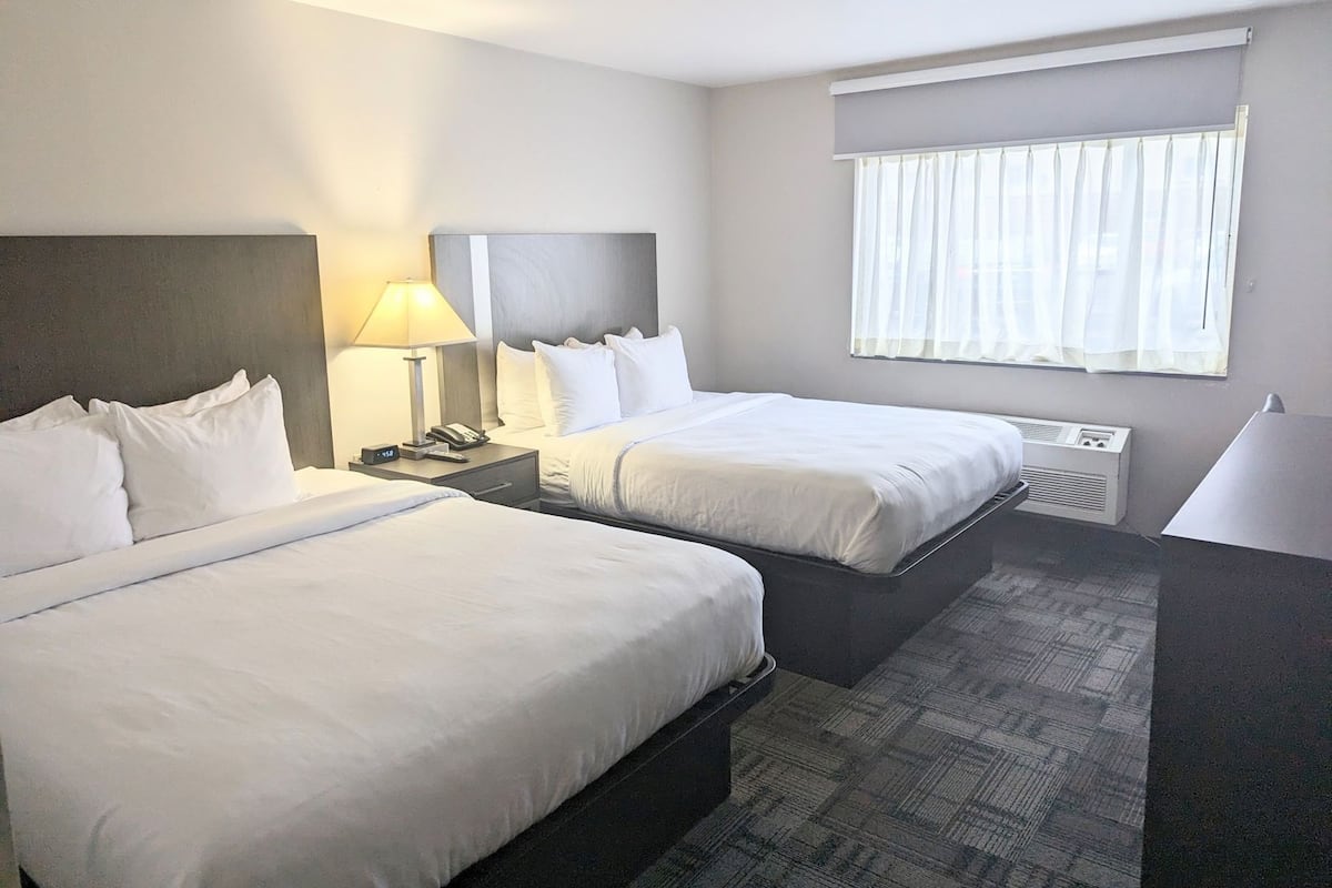 Une chambre d’hôtel avec deux lits, une table de chevet avec une lampe, un téléphone et une fenêtre avec des rideaux.