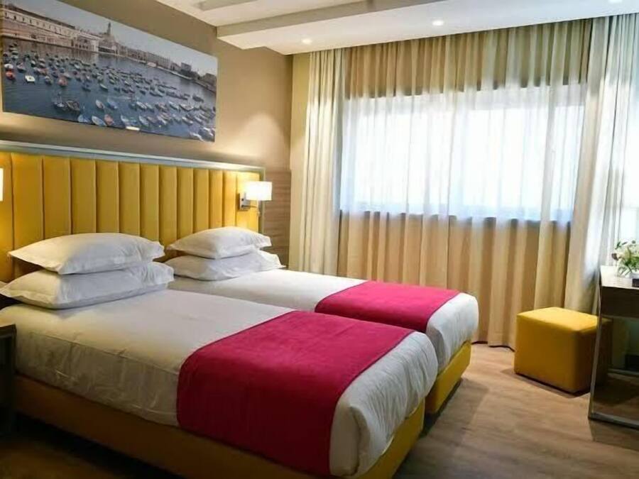 Habitación de hotel con dos camas, un escritorio y una ventana con cortinas.
