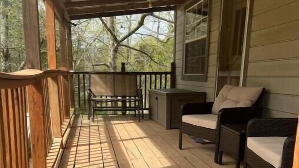 A wooden deck with a patterned rug, outdoor furniture, and a view of trees. - COZY CABIN (Mount Ida)