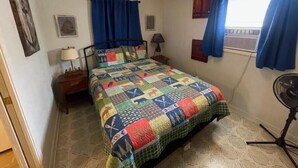A bedroom with a bed, a nightstand, a lamp, a fan, and a window with curtains. - COZY CABIN (Mount Ida)