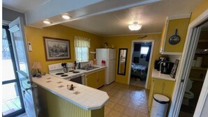 A compact kitchen with a central island, a refrigerator, and a sink. There is a small dining area with a table and chairs. - COZY CABIN (Mount Ida)