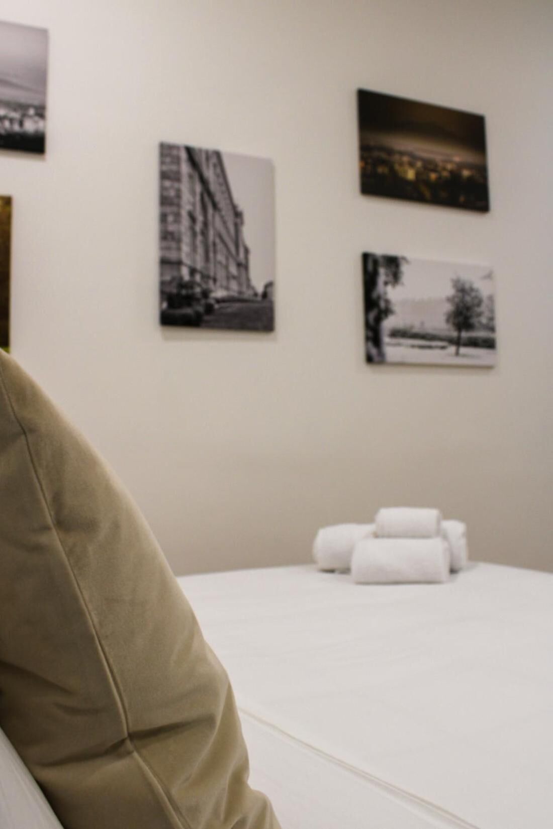Una habitación de hotel con una cama, un almohadón y tres fotografías blanco y negro en la pared.